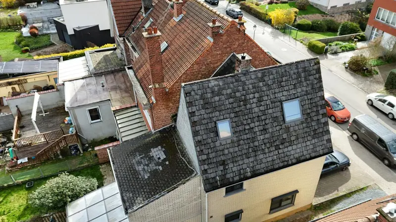 Ancien toit en ardoises artificielles couvert de mousse et rapiécé, annexe plate à côté, vue du drone