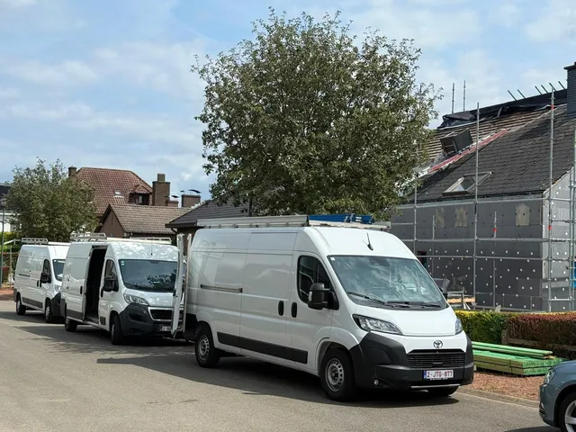 Trois camionnettes blanches de l’entreprise garées devant une maison en rénovation sous échafaudage