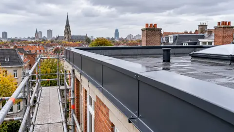 Corniche métallique anthracite posée en rive d’une toiture plate d’immeuble, échafaudage en place