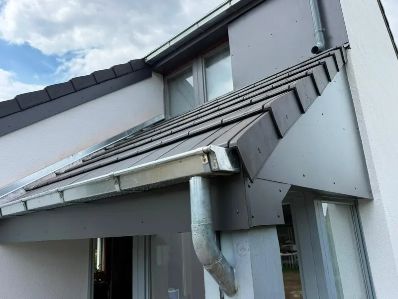 Corniche en zinc neuve avec descente, sous une lucarne habillée de bardage gris, maison rénovée