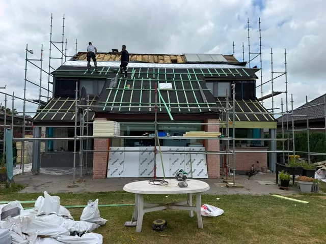 Deux couvreurs sur le toit d’une maison en rénovation, sous-toiture verte et isolant visibles, échafaudage sur trois côtés