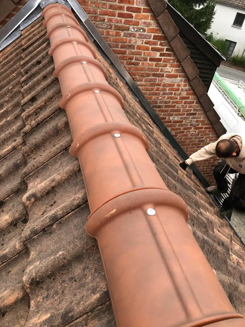 Faîtage neuf en tuiles de terre cuite posé le long d’un mur pignon en briques