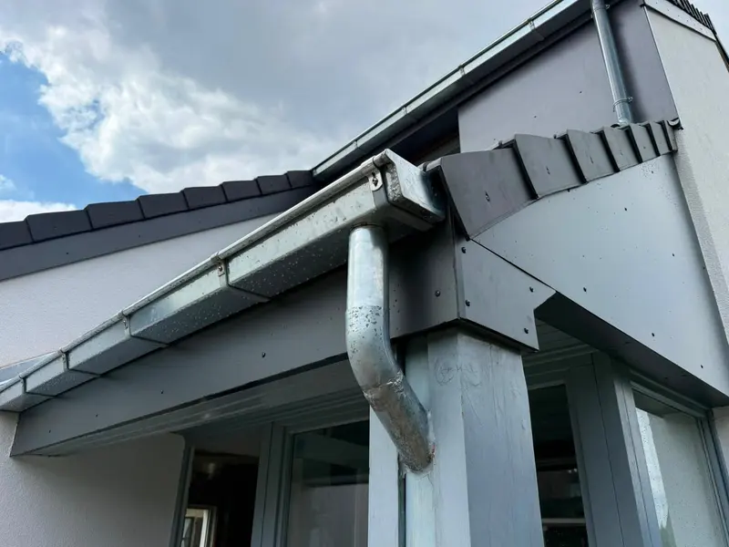 Angle de toiture avec gouttière en zinc, descente et bandeau de rive, vue en contre-plongée