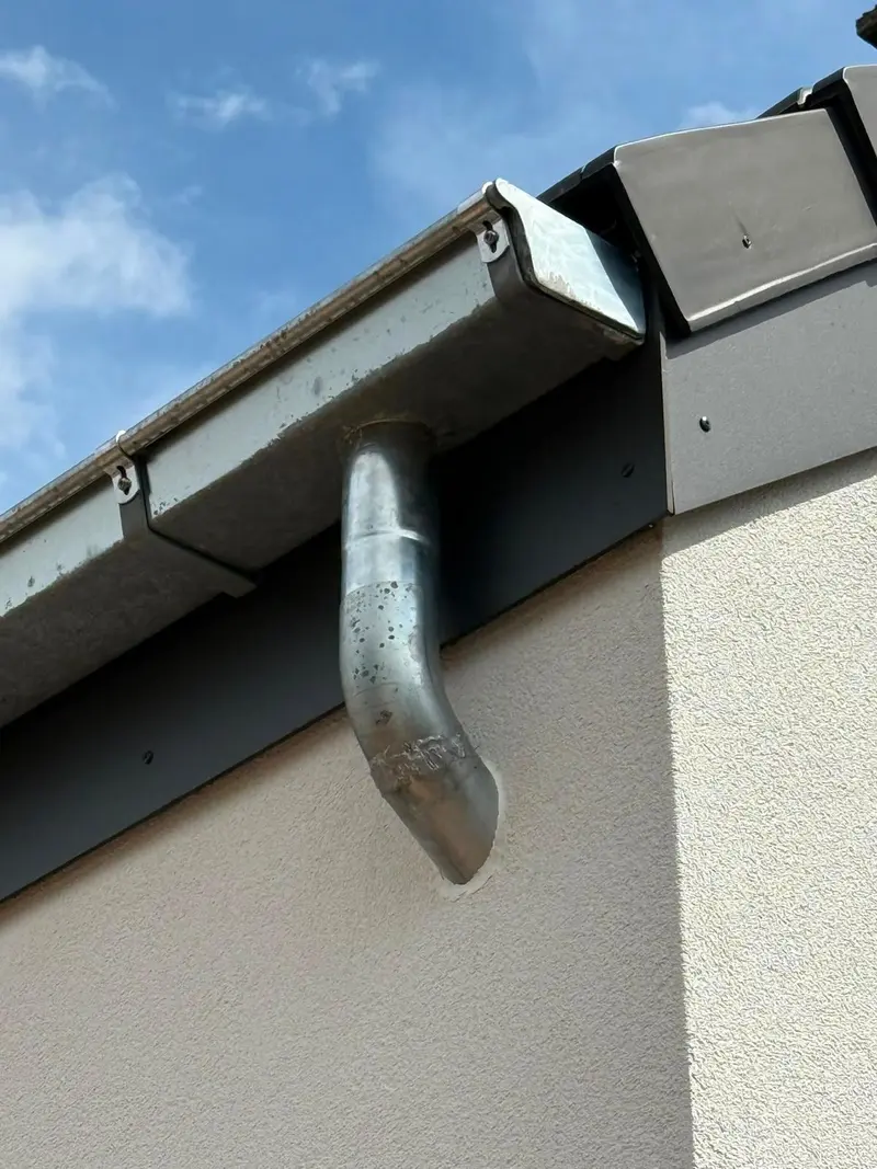 Gros plan sur une gouttière en zinc neuve et sa descente, bandeau de rive gris anthracite sur façade blanche