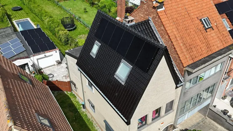 Maison après rénovation : toit en tuiles noires avec fenêtres de toit et panneaux solaires intégrés, vue du drone