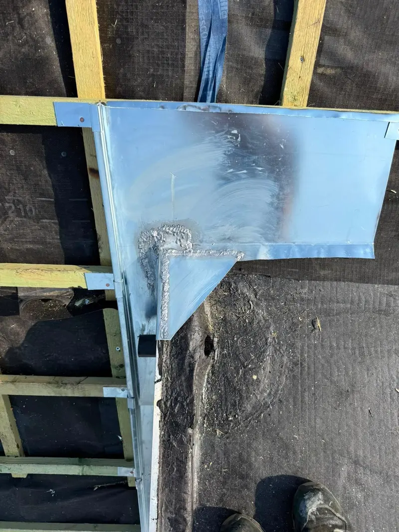 Détail d’une noue en zinc en cours de pose avec soudure, sous-toiture noire et liteaux, chantier