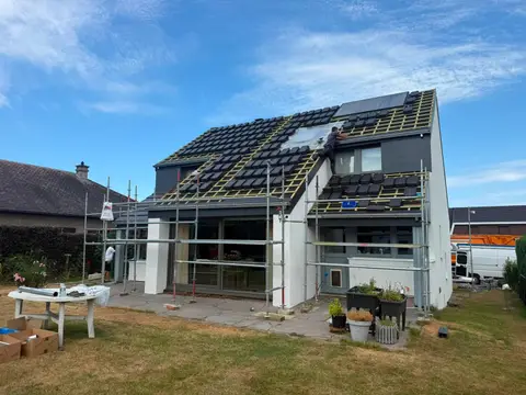 Pose de tuiles plates anthracite sur une maison rénovée, échafaudage, couvreur sur le versant, ciel bleu
