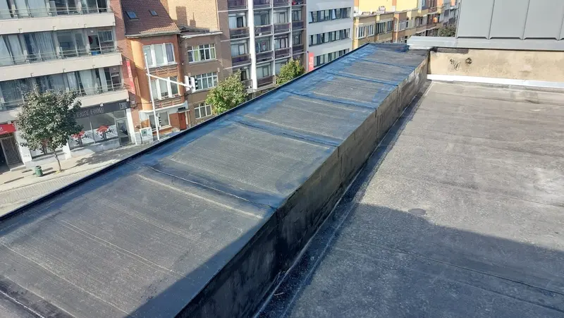 Toiture plate en roofing bitumineux avec son acrotère relevé côté rue, immeubles d’en face