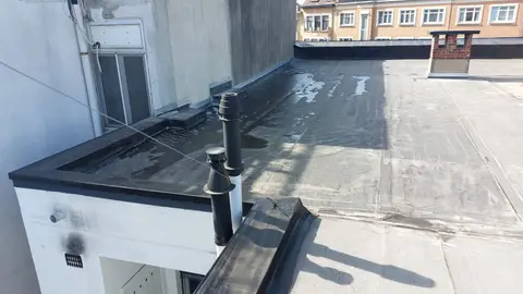 Toiture plate en roofing bitumineux fraîchement posée, avec deux sorties de ventilation, à l’arrière d’une maison de ville