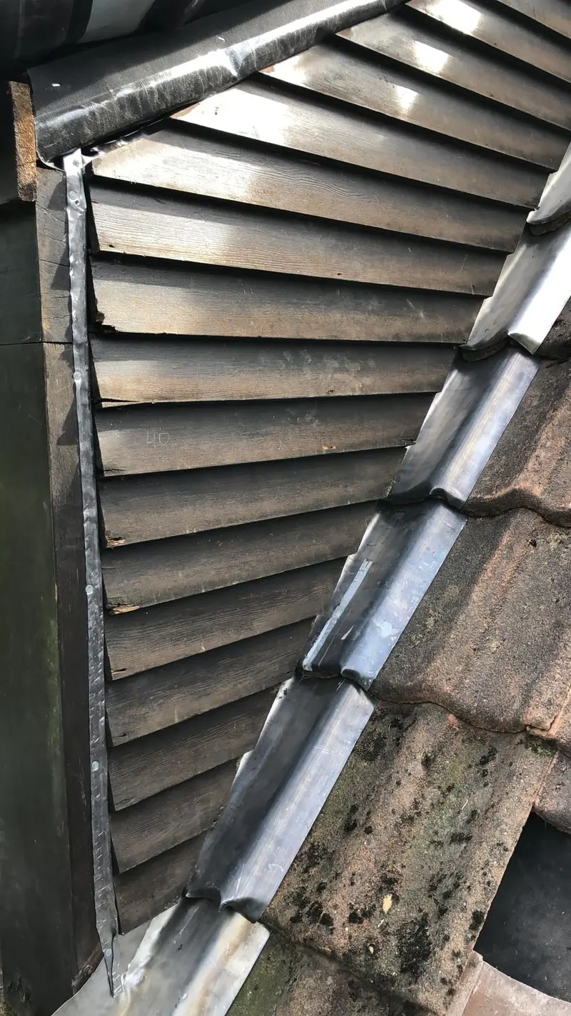 Raccord en zinc entre un mur et un versant de tuiles sombres