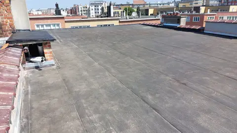 Grande toiture plate d’immeuble en roofing bitumineux, souches de cheminée et bord en tuiles, vue sur la ville