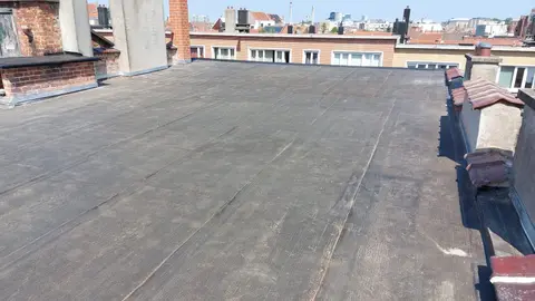 Toiture plate d’un immeuble en roofing, plusieurs souches de cheminée en briques et en béton, horizon urbain