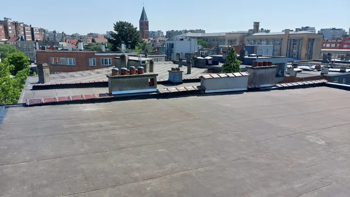 Toiture plate en roofing d’un immeuble, souches de cheminée et clocher à l’horizon