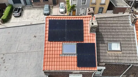 Toiture en tuiles rouges avec fenêtre de toit et panneaux solaires, vue du drone au-dessus d’une rangée de maisons