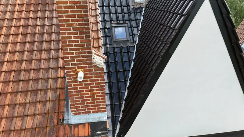 Fenêtre de toit posée dans des tuiles noires neuves, rive en zinc et cheminée en briques, vue du drone